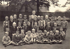 Klassenfoto mit Lehrerin und vielen Jungen in mehreren Reihen auf dem Schulhof