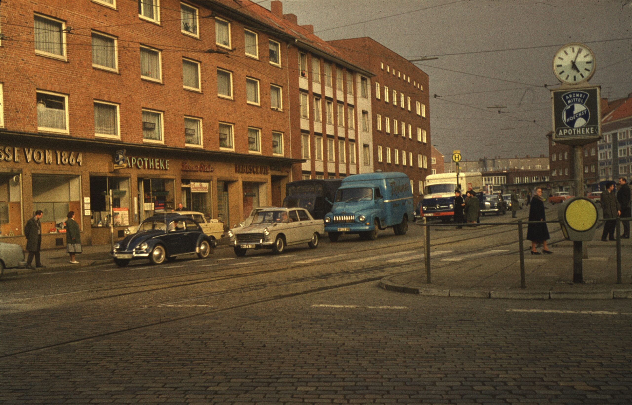 Straßenszene mit alten Autos, Geschäften und Uhr, mit Straßenbahnhaltestelle