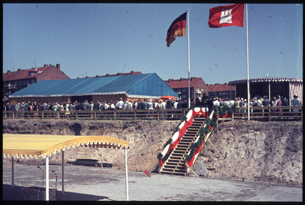 Feier mit blauem Festzelt, rot-weißer Treppe und Flaggen auf Baustelle